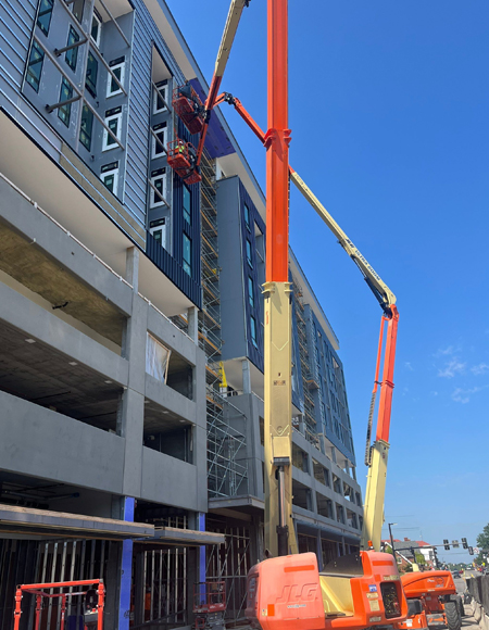 Construction workers using lifts to install exterior materials on a commercial building under construction, showcasing the focus on quality and professional service in exterior solutions.