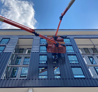 Construction crew using a lift to install commercial exterior siding on a multi-story building, showcasing quality materials and professional installation.