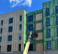 Construction site featuring a lift working on a commercial building envelope, showcasing various exterior elements like wall systems and windows, highlighting integration for weather protection.