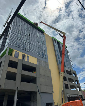 Construction workers using a lift to install exterior building envelope components on a multi-story commercial property under renovation, showcasing various layers including windows and wall systems.