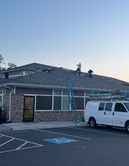 Roofing crew working on a commercial building, with a ladder and service van visible, showcasing exterior construction services by Nastase Contracting.