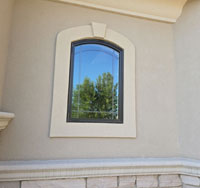 Residential window with arched design, showcasing energy-efficient glass reflecting surrounding trees and exterior wall details, emphasizing quality and aesthetic appeal for home protection.