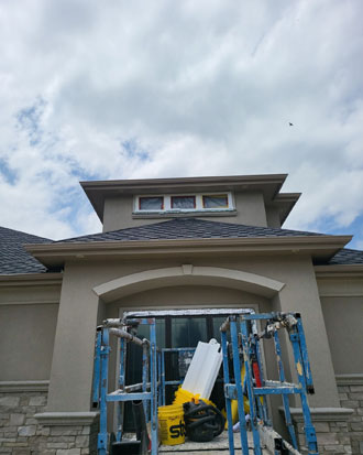 Residential window installation in progress on a house, featuring scaffolding, partially installed windows, and a cloudy sky backdrop.