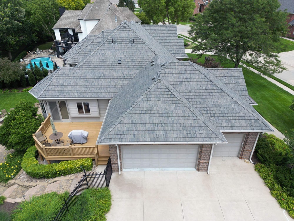 Aerial view of a residential home showcasing a composite roof with a grey color scheme, surrounded by a well-maintained lawn and patio area, highlighting the aesthetic appeal and durability of premium roofing solutions.