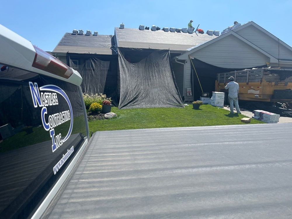 Nastase Contracting crew performing residential roofing installation with Tamko Flex 4 shingles in Weathered Wood on a house in Bennington, Nebraska, featuring protective tarps and materials on-site.