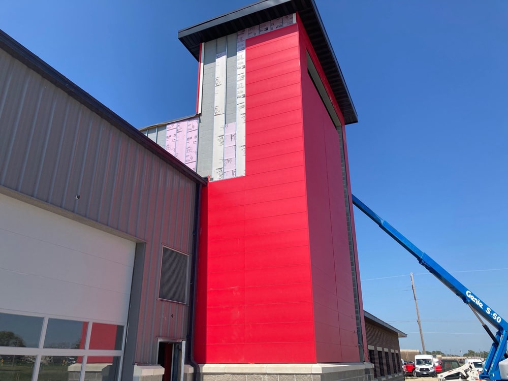 Exterior view of Valley Fire Station featuring fire engine red Nichiha Illumination Panels, with construction equipment in use and clear blue sky.
