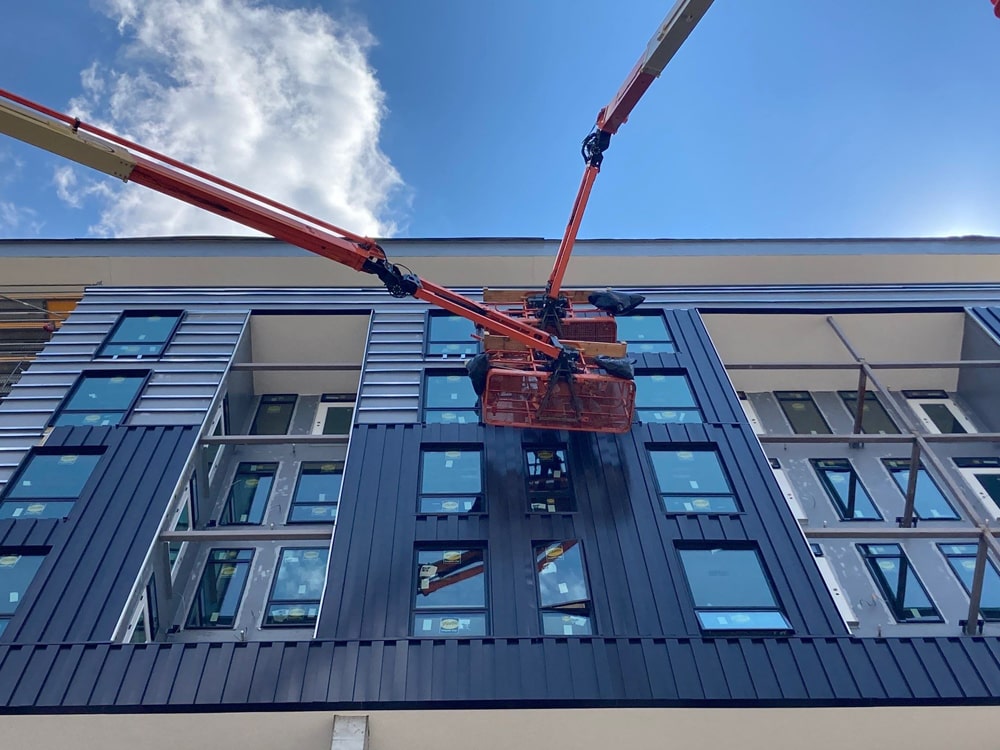 Construction workers using a lift to install Nichiha metal panels on the exterior of the Blackstone Apartments in Omaha, NE, showcasing the building's modern design and height.
