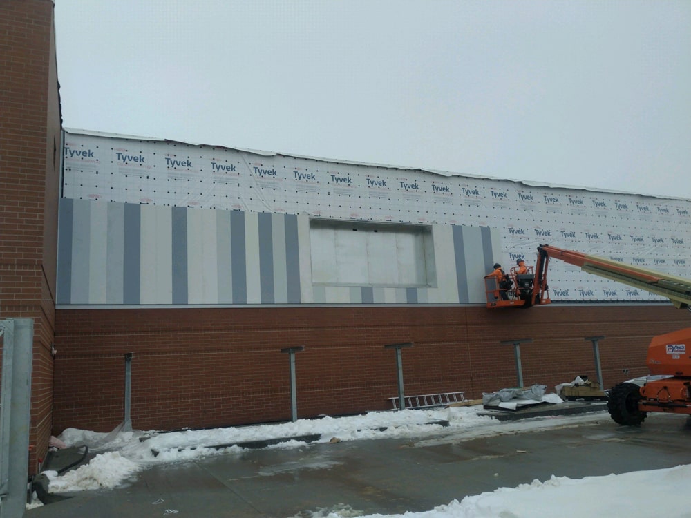 Construction workers applying printed and painted James Hardie board and batten siding on the exterior wall of the Rock Creek Ambulatory Surgery Center in Omaha, NE, with Tyvek sheathing visible above.
