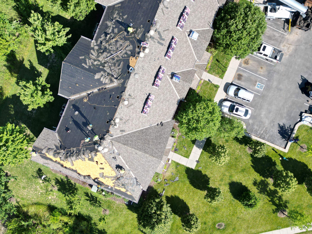 Aerial view of multifamily residence roof under renovation, showing removed shingles and workers, with surrounding greenery and parked vehicles in Omaha, NE.