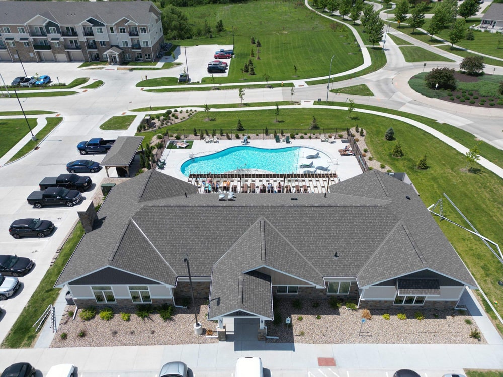 Aerial view of Hanover Flats multifamily property in Bennington, Nebraska, showcasing the commercial roof with Class 4 Impact Rated shingles, surrounding parking area, and poolside amenities.