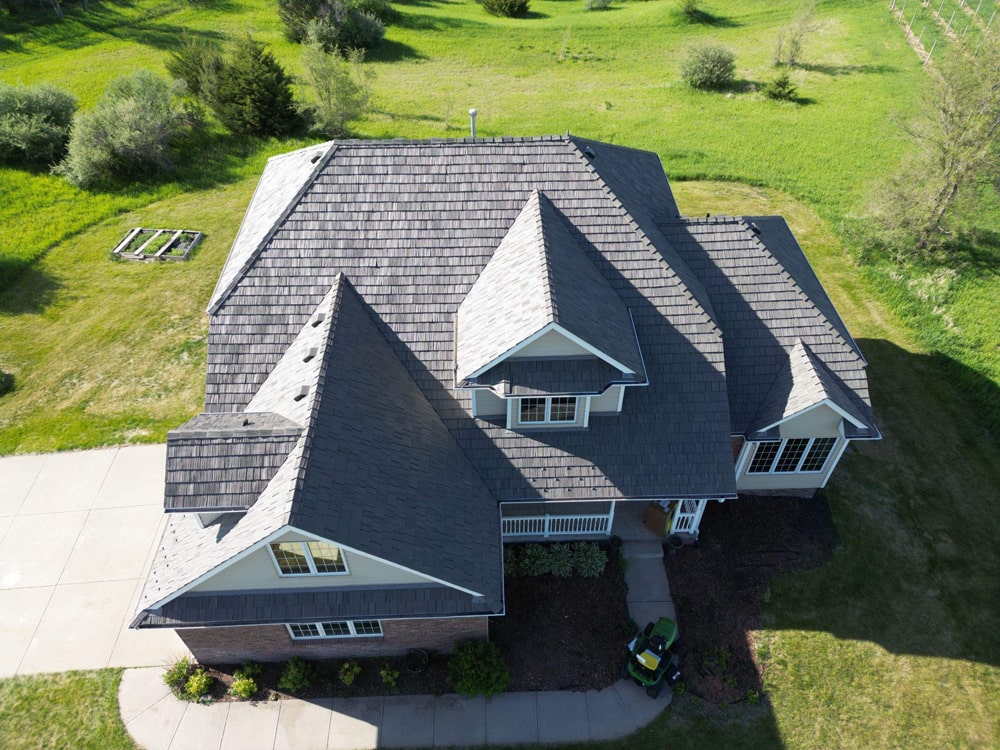 Aerial view of a residential home featuring a composite cedar shake roof, surrounded by green landscaping, illustrating roofing solutions in Omaha.